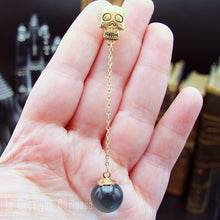 Laden Sie das Bild in den Galerie-Viewer, Boucle d’oreille Les Éthéréennes tenue en main, montrant la chaîne dorée et la perle en verre bleu.