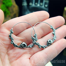 Charger l&#39;image dans la galerie, Boucles d&#39;oreilles gothiques, style créoles, en acier inoxydable. Branche en forme de cercle ornée de petits crânes sur laquelle repose une tête de mort plus grande que les autres. Esprit romantique, memento mori.