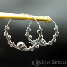 Charger l&#39;image dans la galerie, Boucles d&#39;oreilles gothiques, style créoles, en acier inoxydable. Branche en forme de cercle ornée de petits crânes sur laquelle repose une tête de mort plus grande que les autres. Esprit romantique, memento mori.