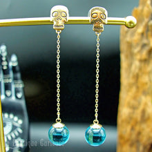 Laden Sie das Bild in den Galerie-Viewer, Boucles d’oreilles gothiques dorées avec crânes et perles en verre bleu, modèle Les Éthéréennes.
