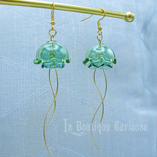 Load image into Gallery viewer, Boucles d&#39;oreilles méduse pendantes dorées en verre et acier couleur rose violet vert. Thème steampunk mer Jules Verne plongée sous marine