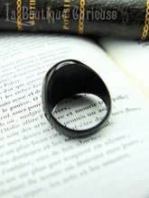 Charger l'image dans la galerie, Bague alchimique en acier noir posée sur un livre ancien, vue de dos.
