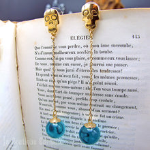 Laden Sie das Bild in den Galerie-Viewer, Boucles d’oreilles gothiques dorées avec perles bleues, posées sur un livre ancien.