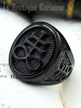 Charger l'image dans la galerie, Bague symbole alchimique croix de soufre en acier inoxydable noir vue de trois quart posée sur un livre.